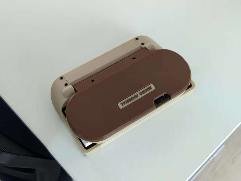 Top-down view of the Micro Journal Rev.6.1 device fully closed on a white table, showing its matte brown protective outer cover.