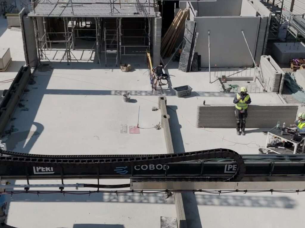 Construction workers standing on a concrete slab floor during the onsite 3D printing process with a COBOD BOD2 printer tracking system.