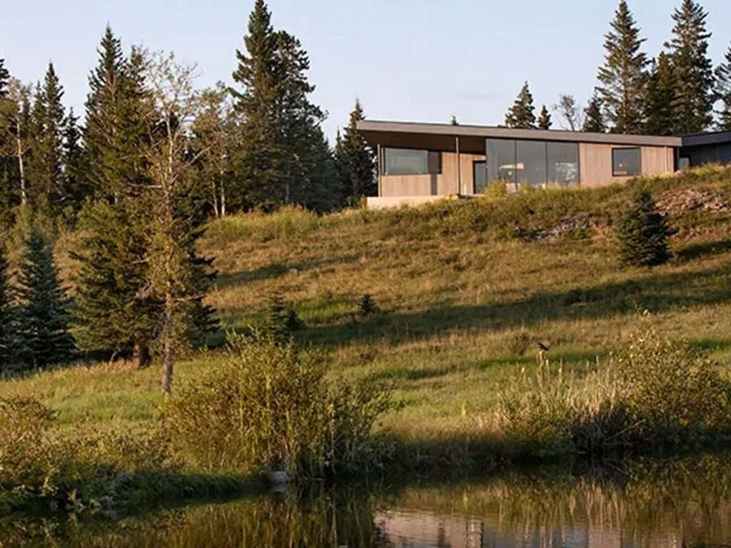 Distant view of Cut Out House sitting on a grassy mountain slope reflecting onto a calm body of water below.