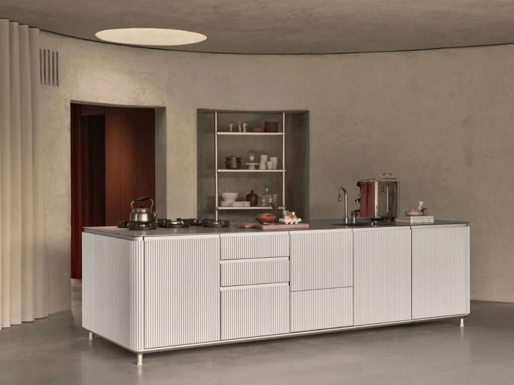 Modern minimalist kitchen featuring a white fluted island unit, concrete walls, and an overhead circular skylight.