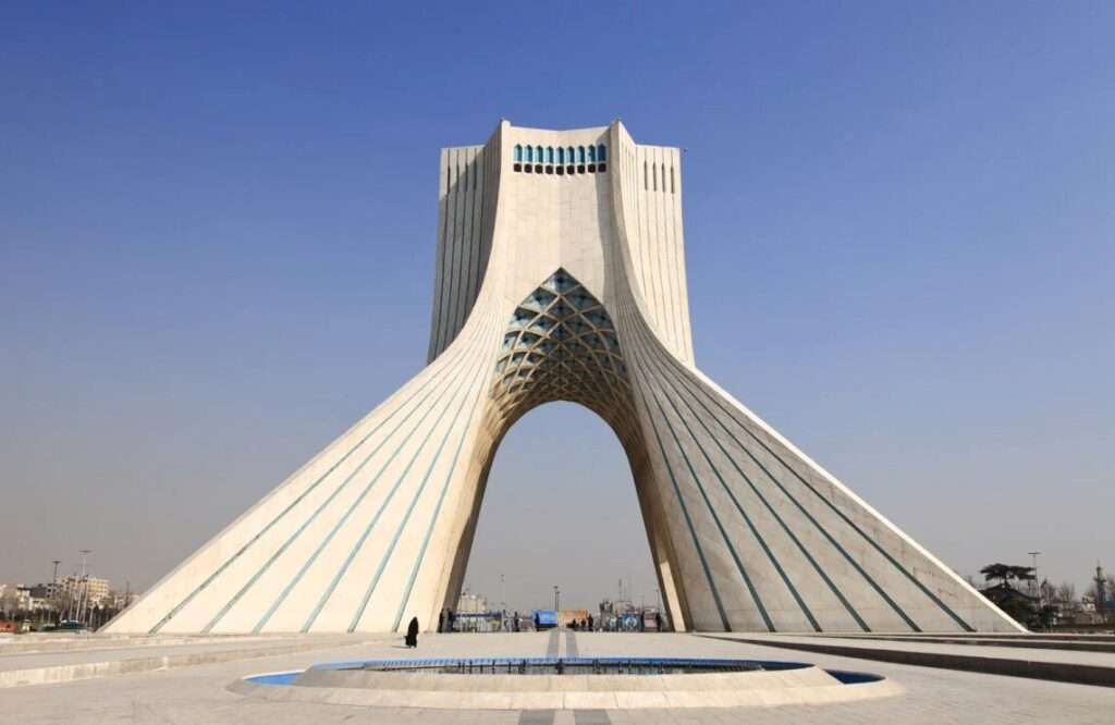 Aerial view of Azadi Tower in Tehran showing the sprawling 68,000-square-meter plaza with its intricate geometric green lawns and surrounding urban traffic patterns.