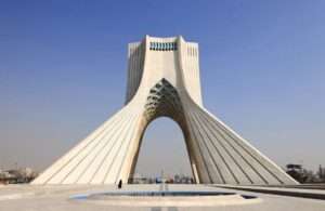 Aerial view of Azadi Tower in Tehran showing the sprawling 68,000-square-meter plaza with its intricate geometric green lawns and surrounding urban traffic patterns.