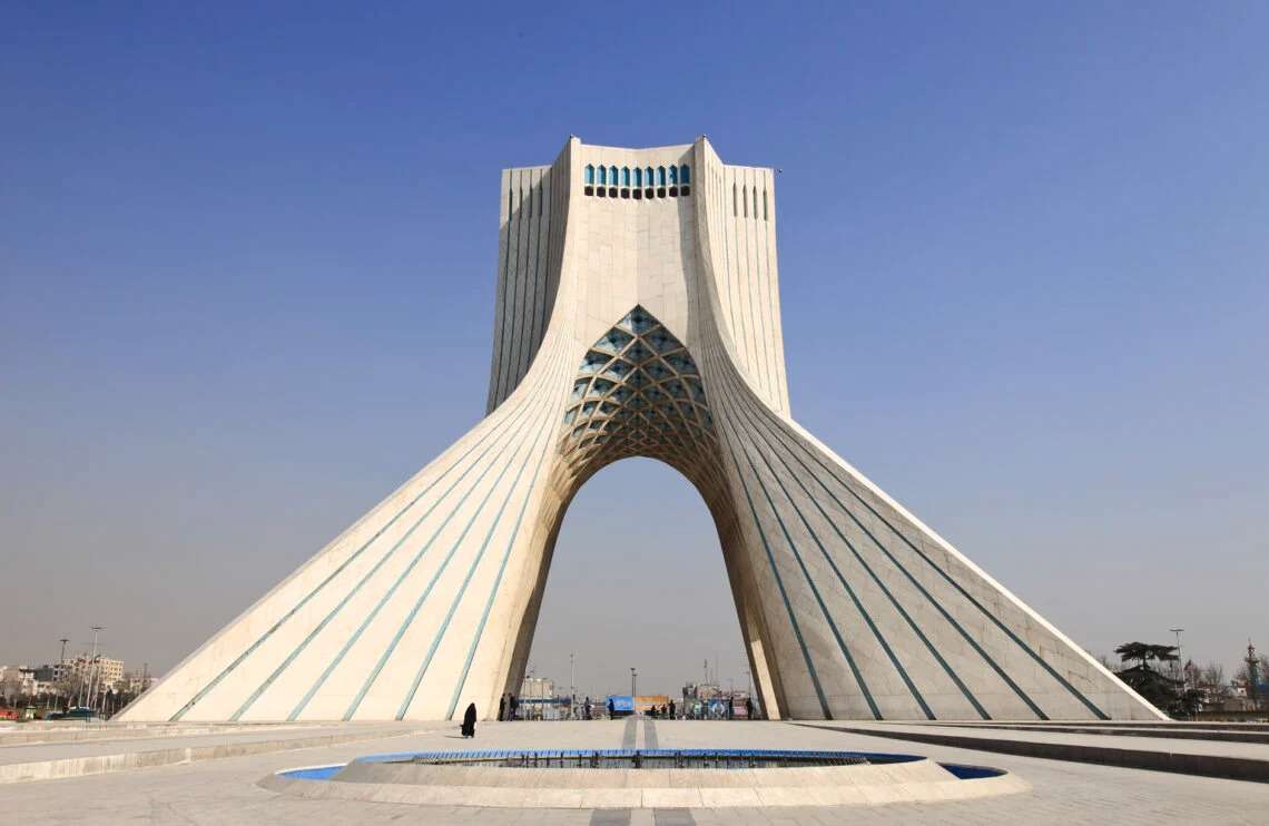 Aerial view of Azadi Tower in Tehran showing the sprawling 68,000-square-meter plaza with its intricate geometric green lawns and surrounding urban traffic patterns.