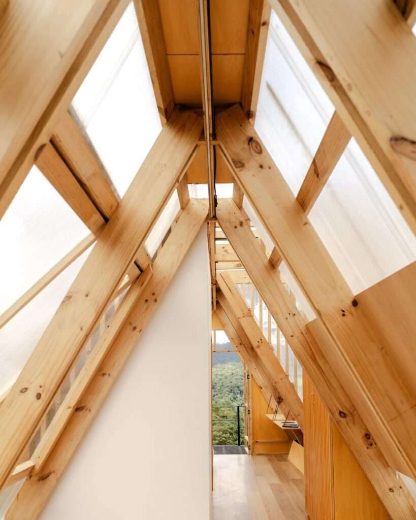 A low angle shot of Casa 6-3 cabin at dusk with warm glowing interior lights filtering through semi-transparent polycarbonate walls, built on a raised black steel platform in Mindo forest.