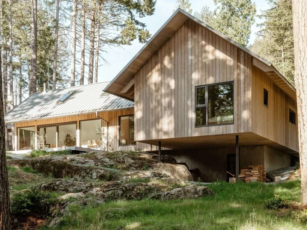 Exterior view highlighting the structural cantilever of the Floating House, where a wooden volume is suspended above a concrete foundation and a rugged rocky slope, supported by steel columns.