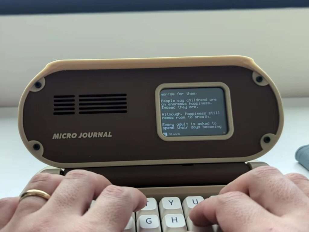 Close-up of a writer typing on the mechanical keyboard of the Micro Journal Rev.6.1 with paragraphs of text visible on the small screen.