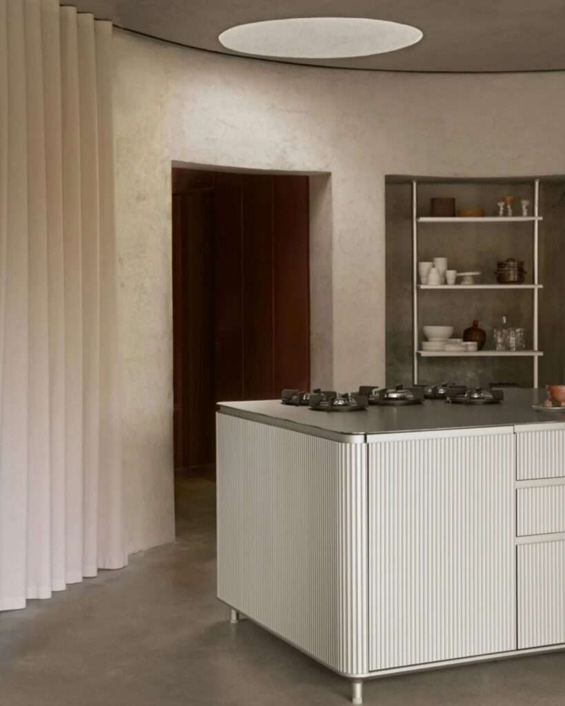 Close-up of a fluted white kitchen island next to a raw concrete doorway and minimalist shelving.