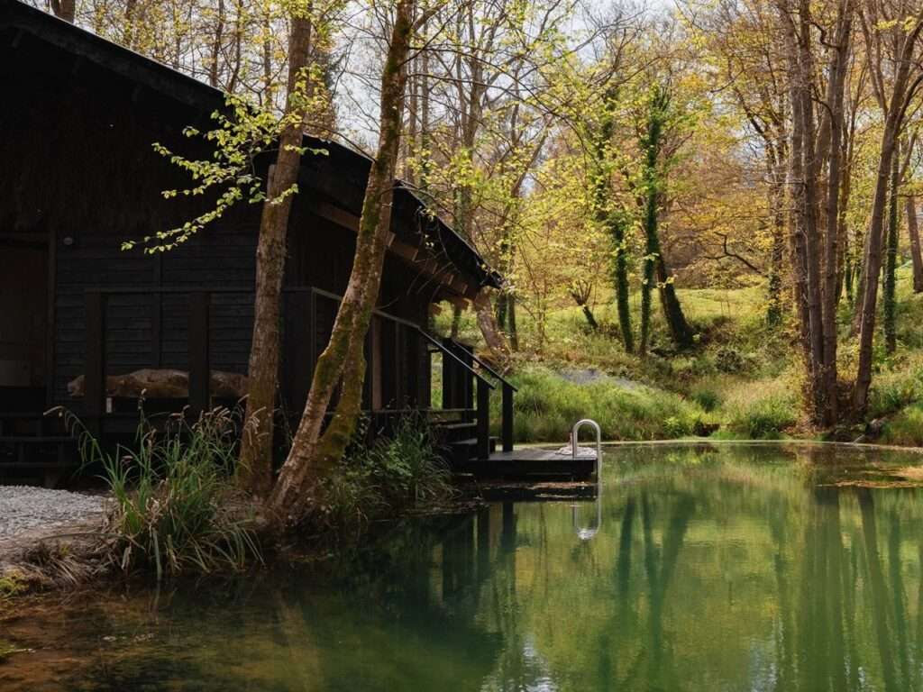 Architectural corner detail of Yogi's Cabin showing the dark charred timber cladding and structural columns next to clear pond water.