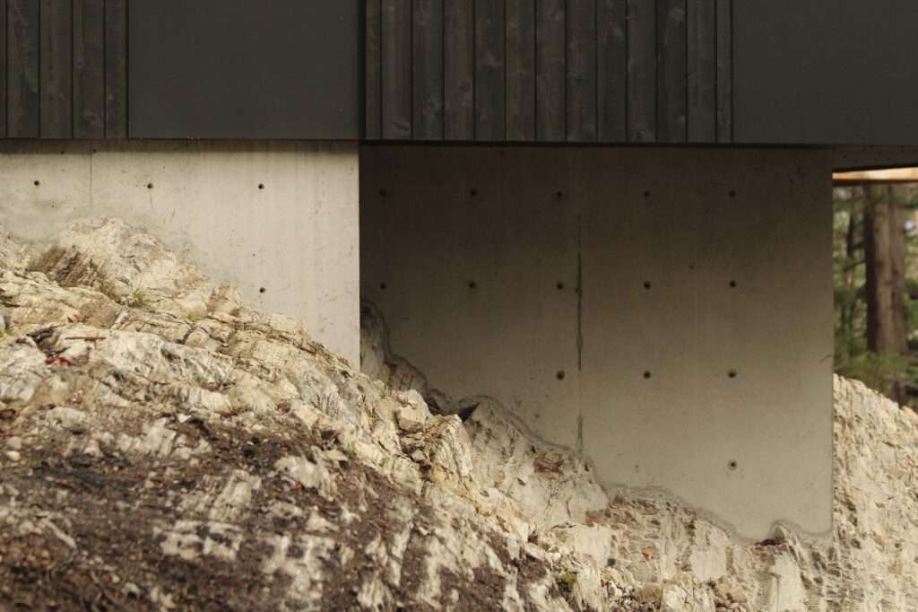 Poured concrete foundation wall anchored directly into native stratified coastal rock formations beneath Hilltop House.