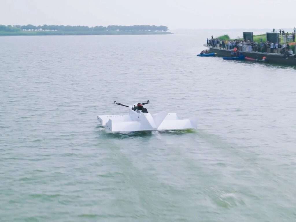 Rear view of the Navee WaveFly 5X moving away from a lakeside pier lined with spectators watching the public flight test.