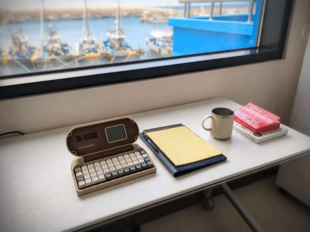 Close-up of the Micro Journal Rev.6.1 device interface featuring a digital animated face on its small IPS display screen above a mechanical keyboard.