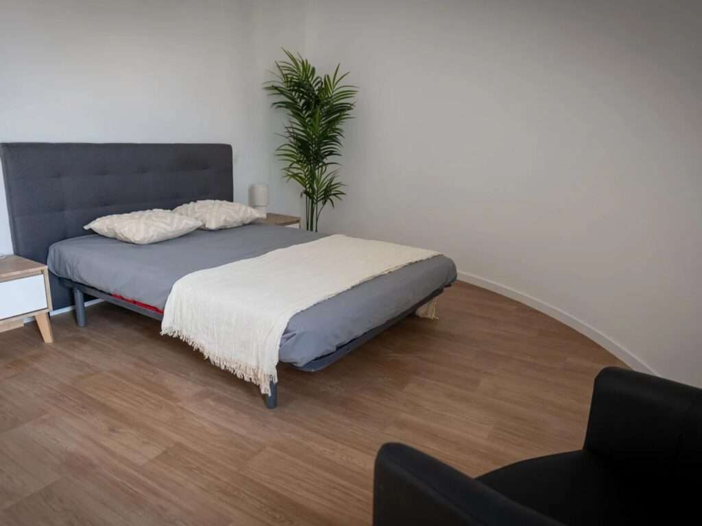 Interior of a finished bedroom in the ViliaSprint2 building showing a modern bed layout against a smooth curved structural wall.