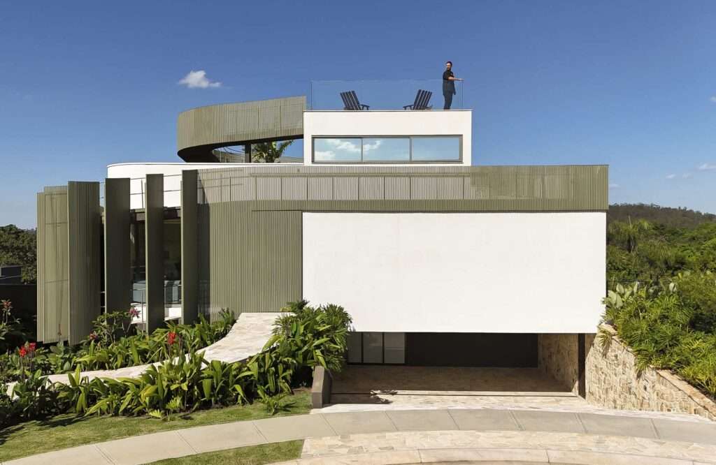 Full exterior shot of Casa Circular with motorized metallic shutters partially opened like petals on the left side, a central white volume, and a person standing on the rooftop observation garden.