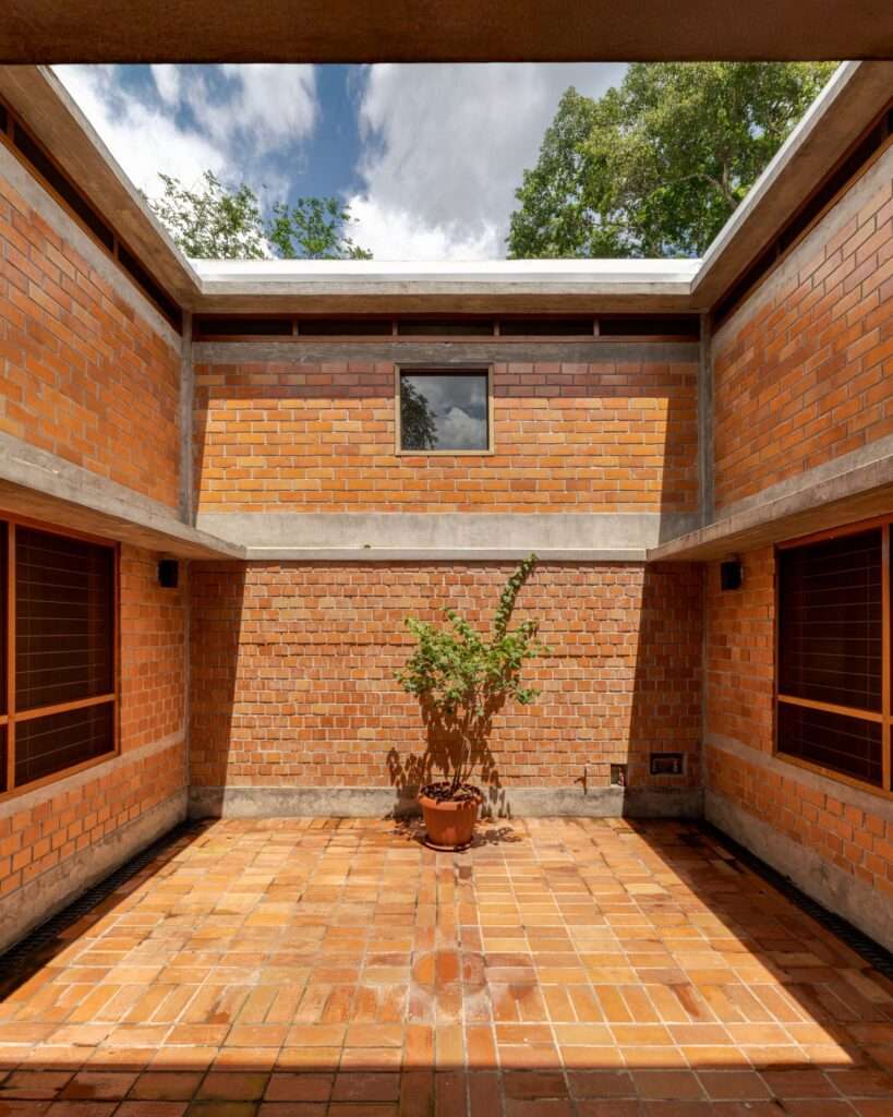 Symmetrical central brick courtyard inside Villa E open to the sky, containing a single potted plant under a bright blue sky.