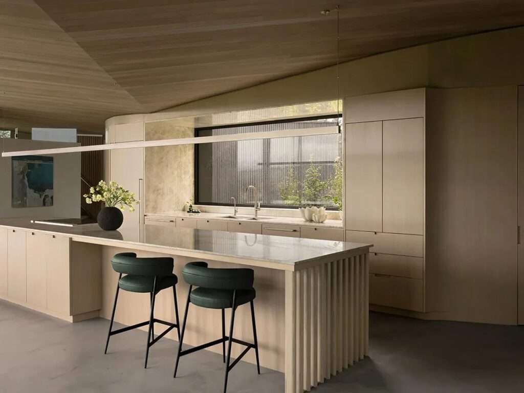 Sleek minimalist kitchen with light wood cabinetry, a marble island bar, and an elongated linear pendant light.