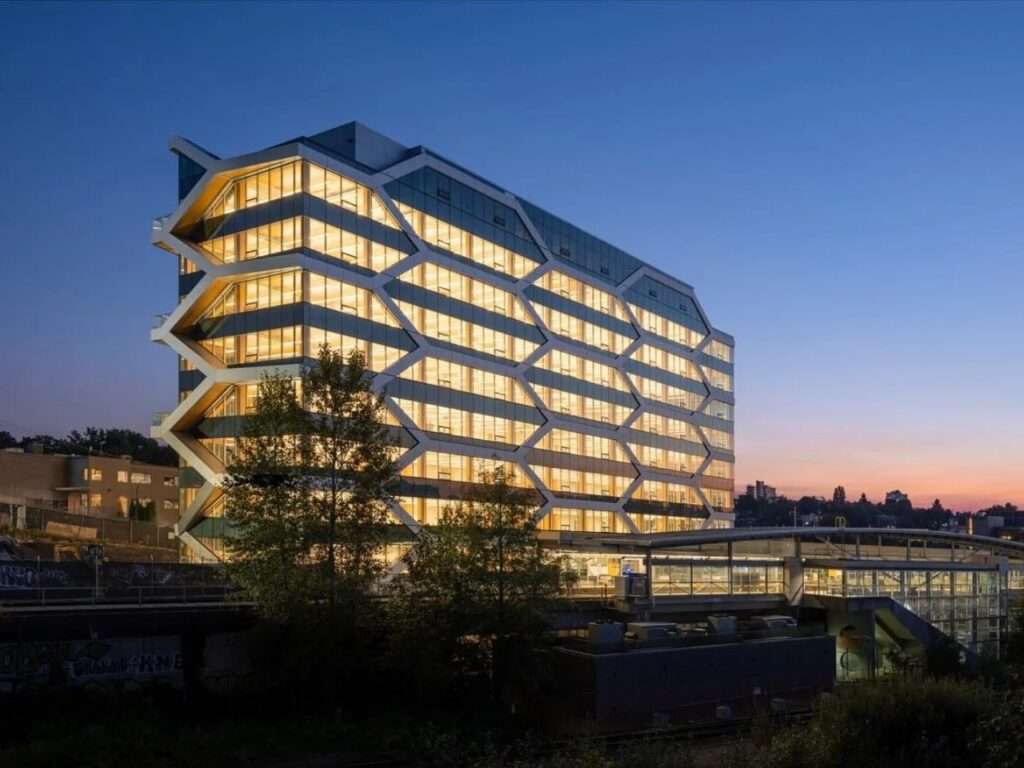 Wide angle view of The Hive mass timber building in Vancouver at night, set against the cityscape.