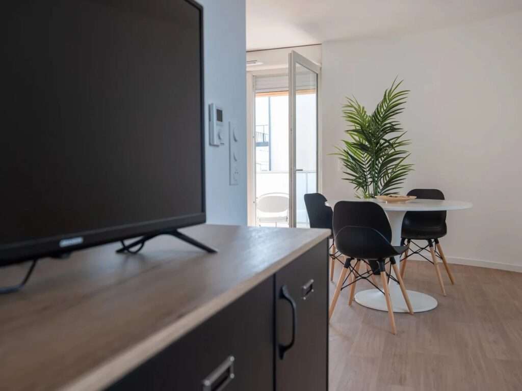 Living area interior view featuring a small dining table, chairs, and a television stand inside a completed apartment unit.
