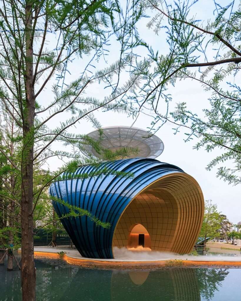 Low-angle view of the blue aluminum-clad Whale Gate structure showing a golden central staircase ascending toward a white disc canopy against a clear sky.