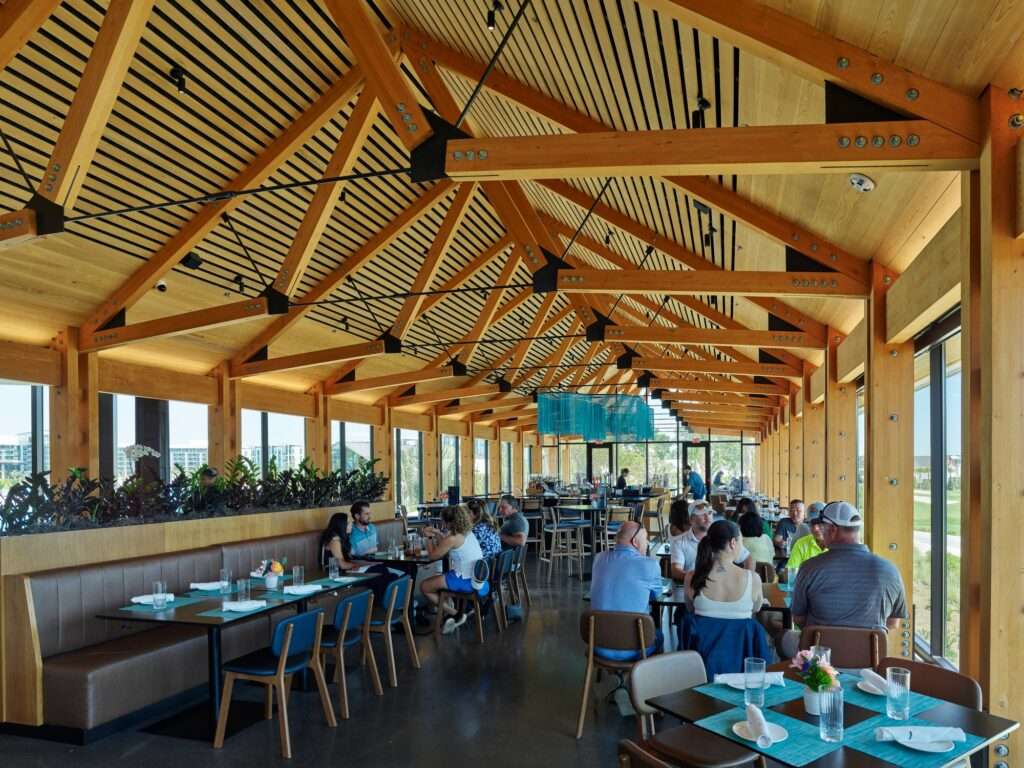 Interior restaurant dining hall under an exposed inverted timber truss roof structure filled with visitors.