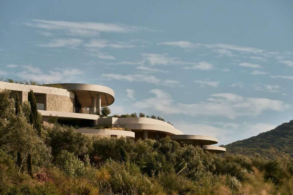 Outdoor dining patio under a concrete canopy featuring woven chairs and a stone table overlooking Navarino Bay.