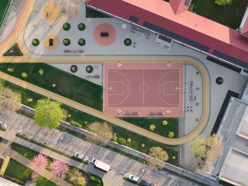Aerial view of a school campus showing a newly paved courtyard, a dedicated basketball court, and surrounding green spaces.