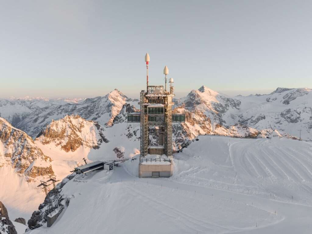High-angle wide shot of the Titlis mountain station project surrounded by expansive snow-covered peaks during sunset.