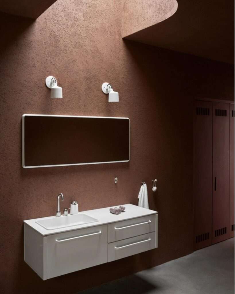 Minimalist bathroom vanity against a textured terracotta-colored wall under a curved skylight.