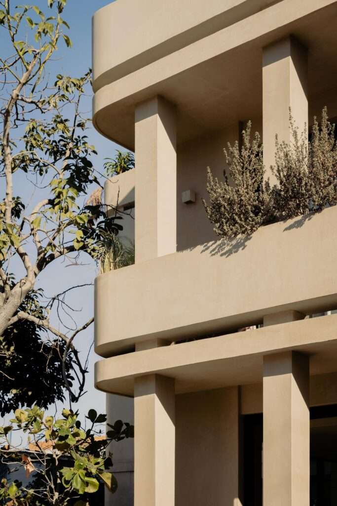 Angled architectural view of Estero Residences balconies showing integrated desert grasses, microcement textures, and tree branches under a clear blue sky.