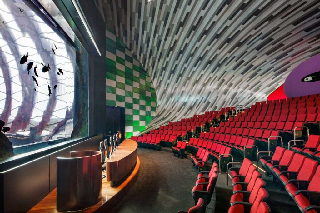 Interior view of the auditorium at Pantanal Biopark featuring red seating and a wall display of aquatic habitats.