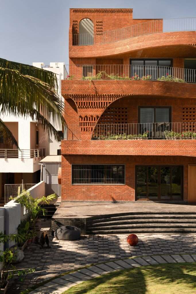 An angled, close-up exterior view of the ground floor stone-paved patio leading up to the curved brick overhangs and main wooden entrance door.