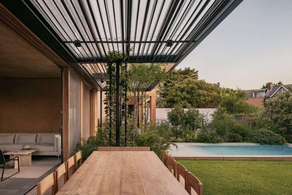 View from the interior of JR House looking out to the covered outdoor terrace, wooden dining table, and swimming pool.