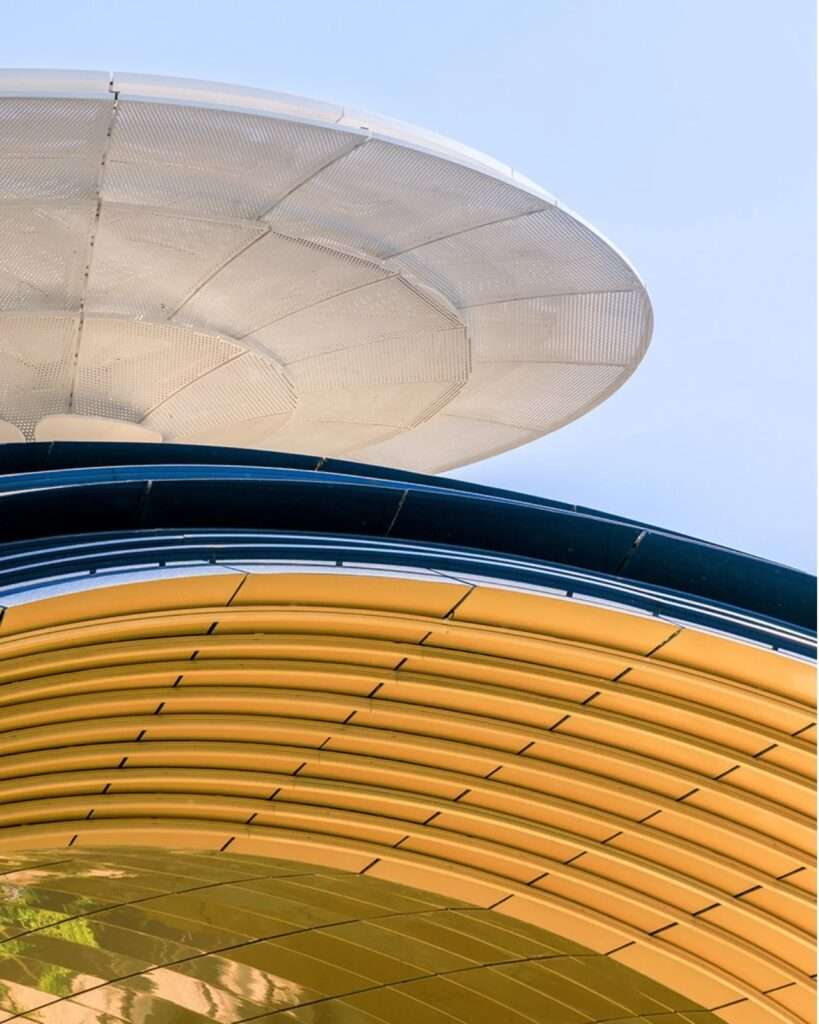 Detail shot looking up at the curved underbelly of the golden arched gateway, with green tree branches visible on the left.