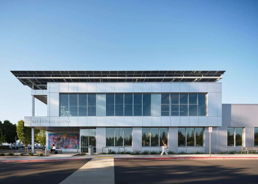 Symmetrical architectural view of the operations center front facade highlighting the large glass windows, silver corrugated metal cladding, and an integrated public book store entrance on the left.