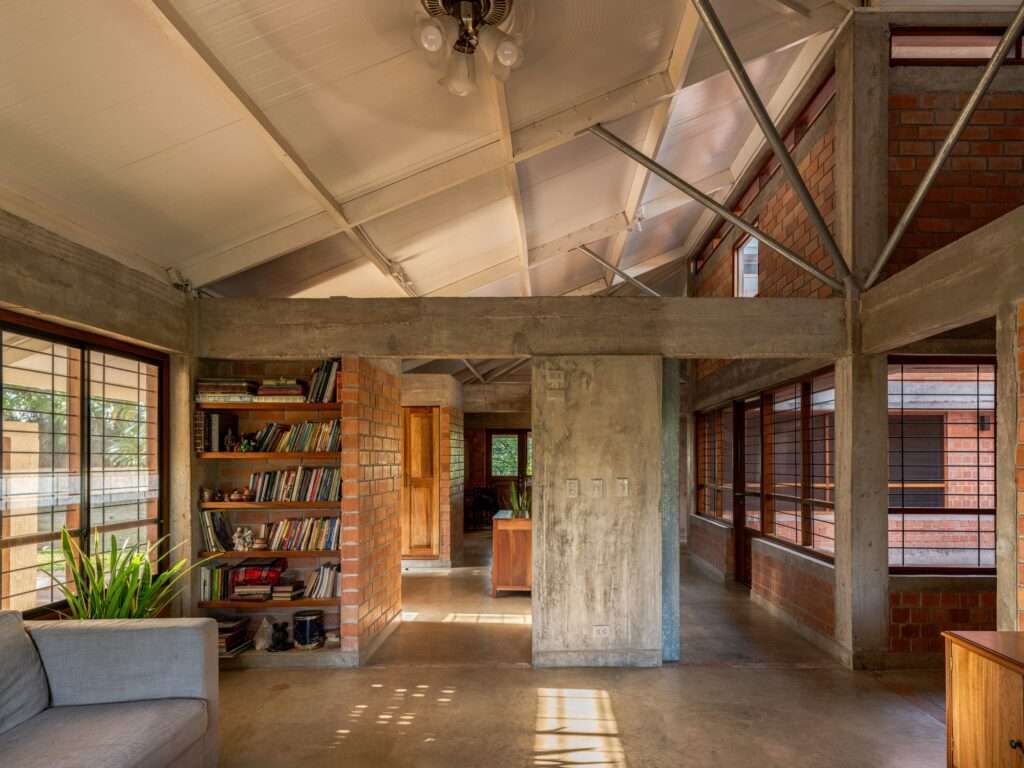 Open-plan living room inside Villa E with concrete columns, a built-in timber bookshelf, and view toward a central courtyard.