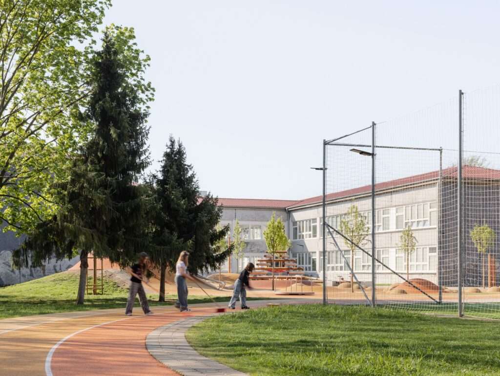 Students in a school yard near a climbing structure, with a running track visible in the background.