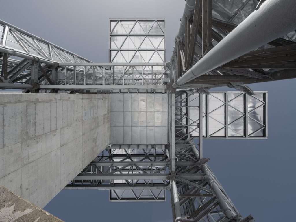 Looking directly upward from the base of the Titlis tower showing the concrete core, steel trusses, and glass cantilevers.