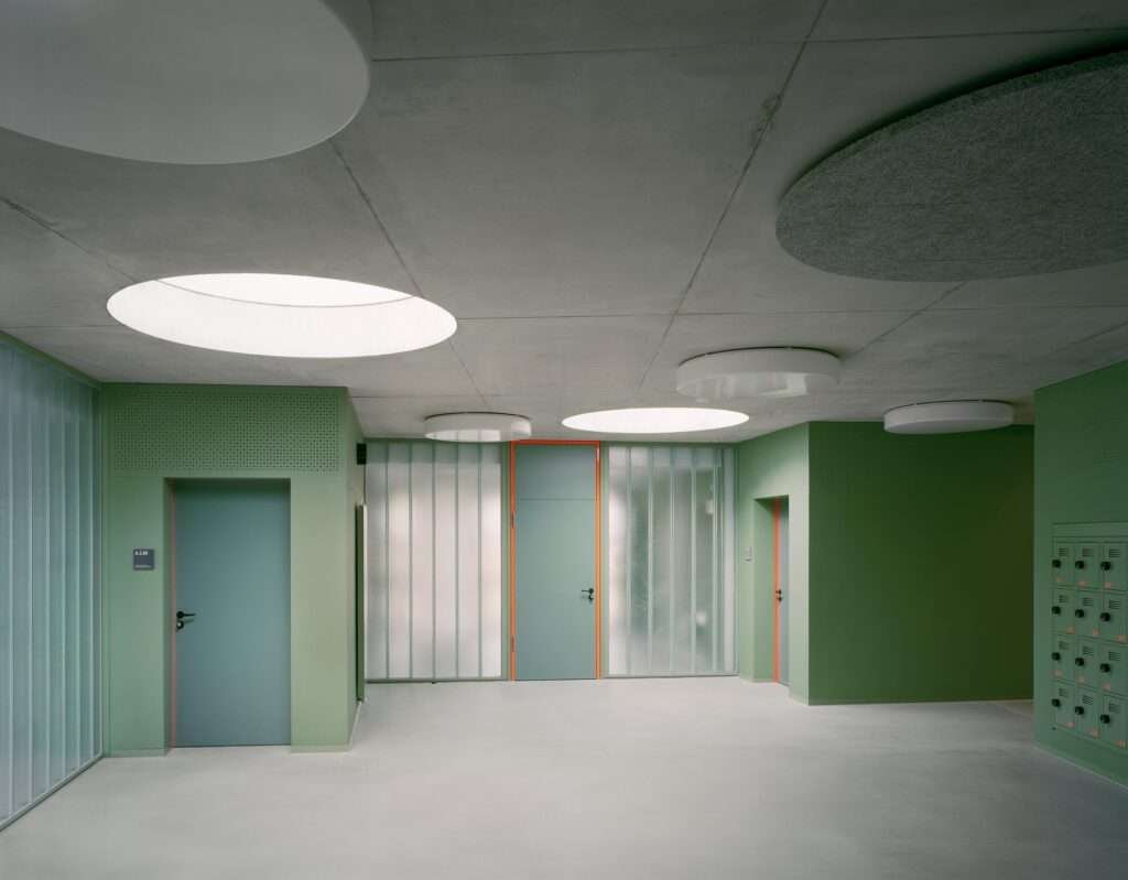 Interior circulation hall with green walls and circular ceiling lights in the Lew Tolstoi School.
