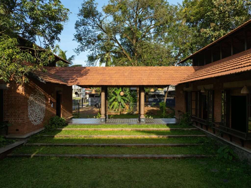 Daytime view of the open-air stepped grass amphitheater between brick pavilions under a clear blue sky.