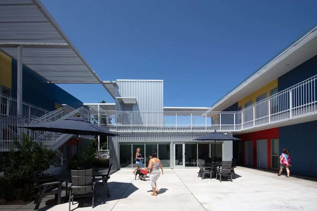 Close-up architectural shot of a two-story residential building with white and grey facades, large glass doors, and a metal overhead trellis.