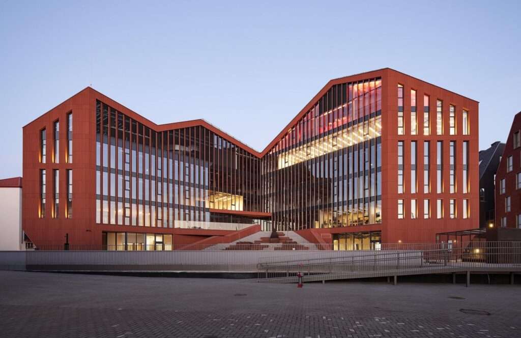 Twilight photograph of the inner courtyard of the HANZA building, showcasing illuminated glass walls, a multi-level public amphitheater with integrated stairs, and a central social courtyard.