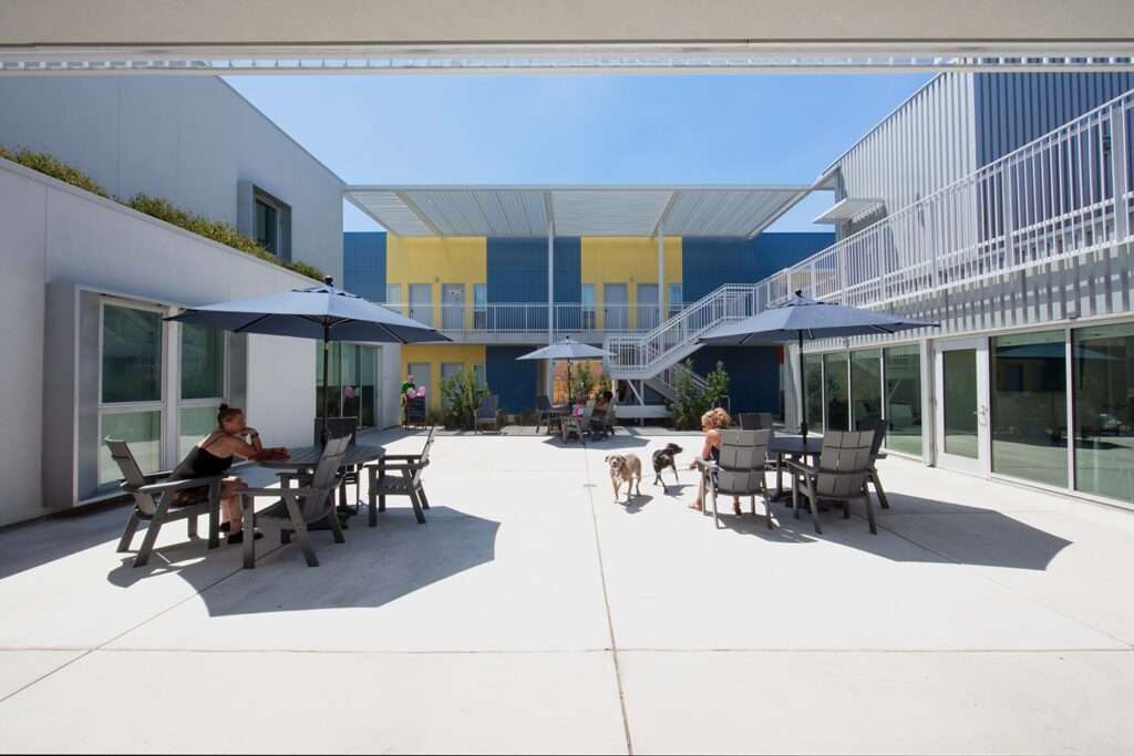 Symmetrical view of a white stucco building facade with three square windows and an open breezeway tunnel leading to an inner courtyard.