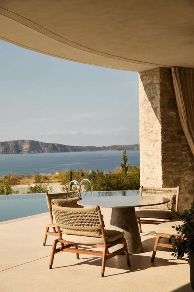 Earth-sheltered stone villas of Mandarin Oriental Costa Navarino terraced into a lush green hillside under a blue sky.
