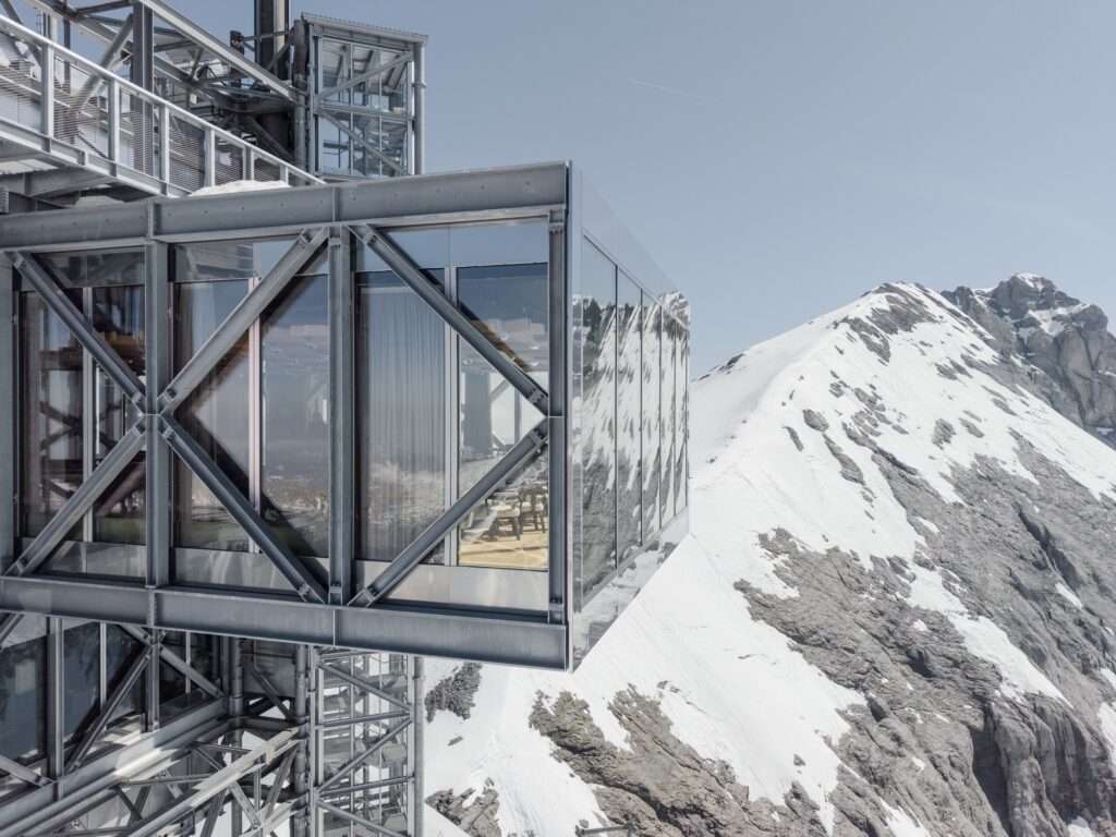 Detailed view of the cantilevered glass volume of the Titlis tower with visible interior seating against a snowy mountain peak.