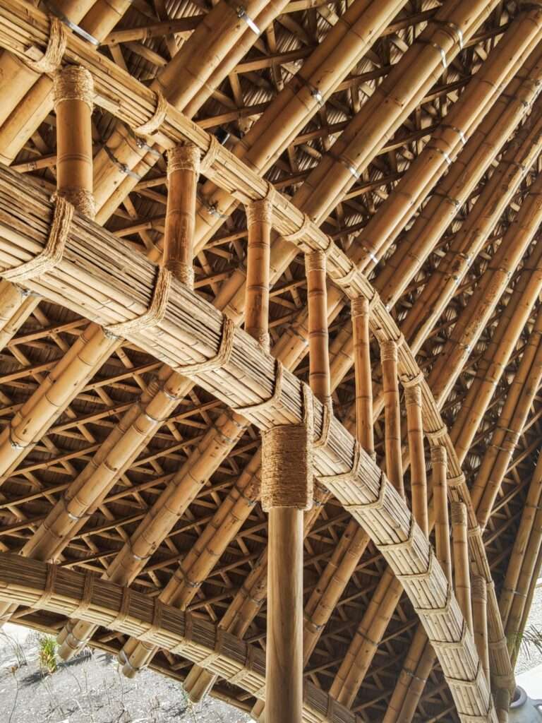 Upward perspective of the intricate interior ceiling framework of CORA Villa, constructed from layered and bound structural bamboo poles.