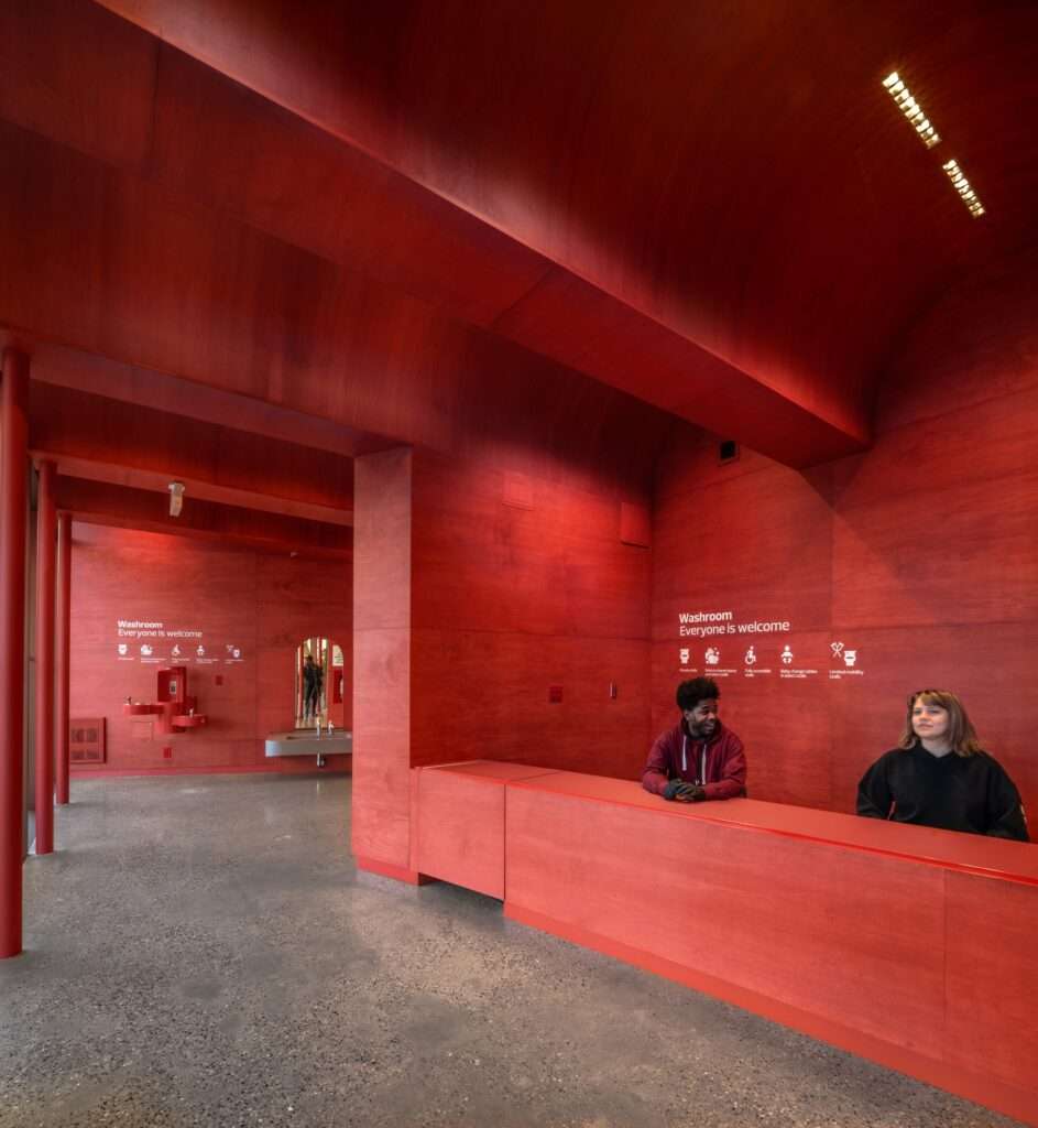 People gathered at the information desk inside the bright red, open-plan interior of the O-day'min Park Pavilion.