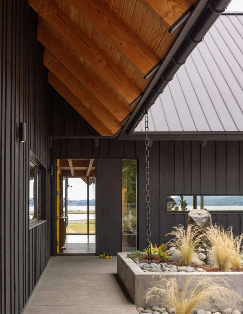 Protected outdoor concrete patio with rain chains and native grass planters looking out to the sea.