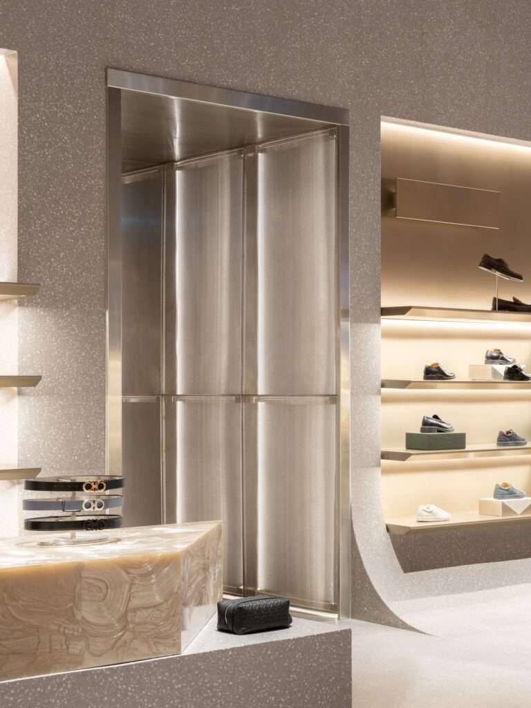 Interior detail showing a textured terrazzo wall curving into the floor alongside a metallic mesh partition and geometric stone display cases.