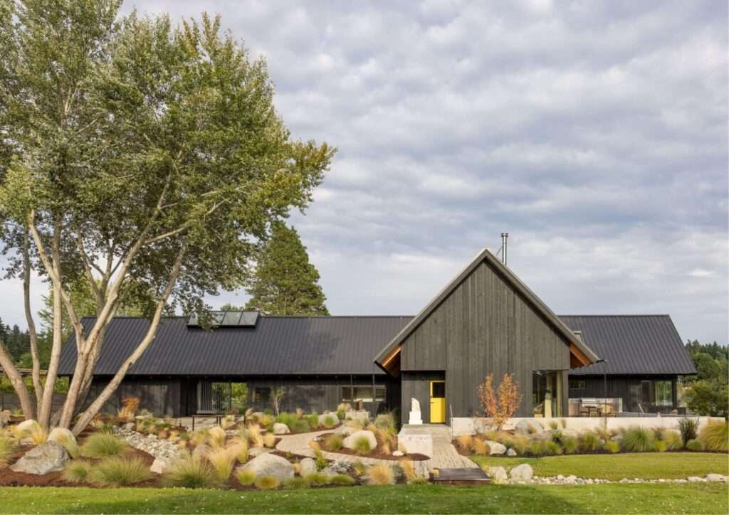 Side view of Day's Inlet House featuring a bright yellow front door, concrete walkways, and dark wood siding.