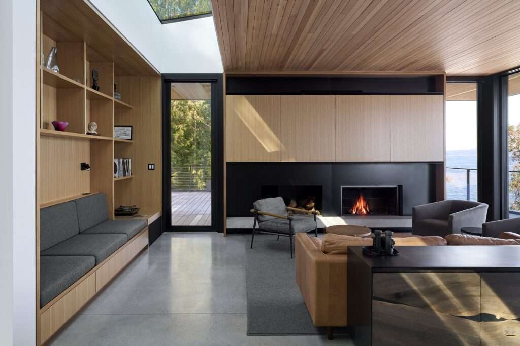 Cozy living room interior with a fireplace, custom wooden cabinetry, and large windows looking out to the sea.