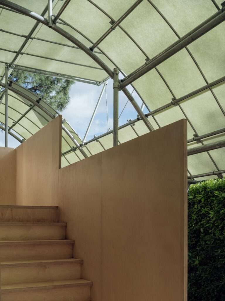 Interior view looking up at the wooden staircase and the geometric steel framework under the translucent canopy of Cabane 7L.